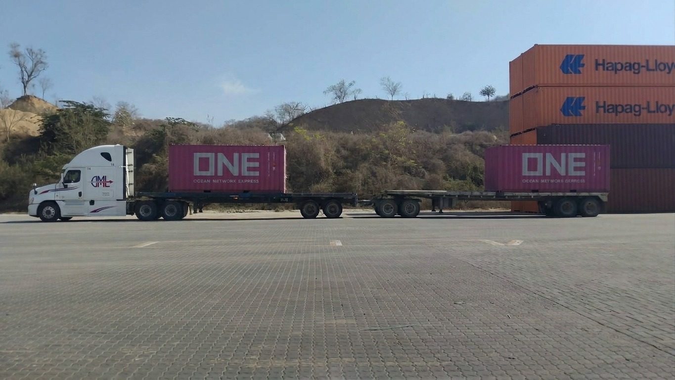 Tractocamión de DML con dos contenedores ONE sobre plataforma en un patio portuario